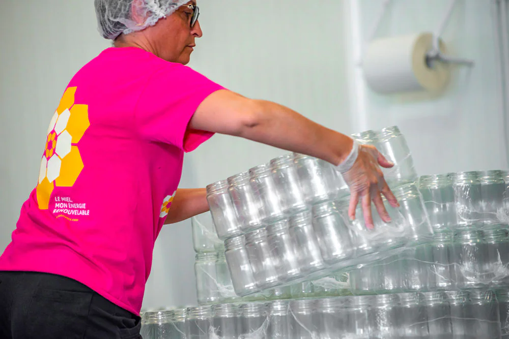 Opératrice manipulant des empilements de pots en verre pour le conditionnement du miel