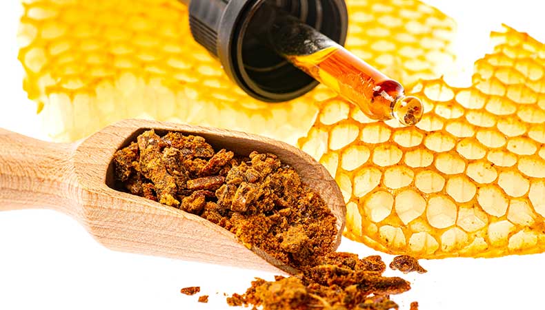 Propolis et teinture de propolis – un concentré naturel de la ruche Propolis brute dans une cuillère en bois et goutte de teinture de propolis sur fond de cire d’abeille